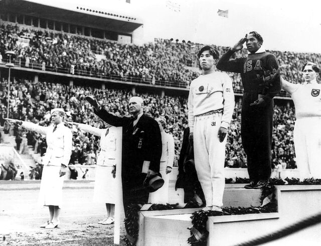 Americký atlet Jesse Owens na stupních vítězů (uprostřed) poté, co vyhrál zlato ve skoku do dálky na olympijských hrách v roce 1936 v Berlíně.
