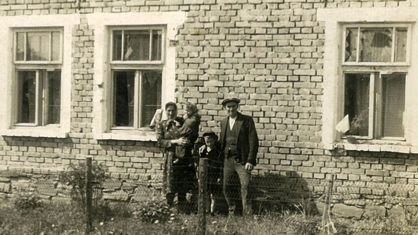 Rodiče Rostislava Čapka s jeho sourozenci před jeho rodným domem v Tršicích, na kterém je vidět poškození od granátů. Foto: Paměť národa