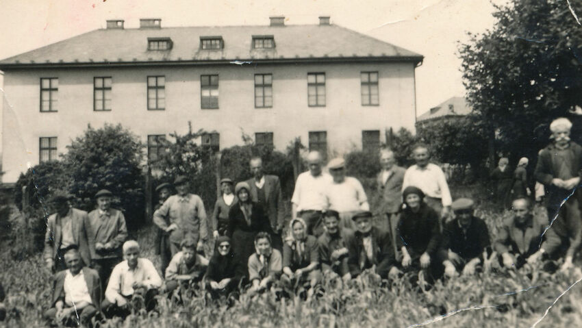 Řečtí uprchlíci před budovou kasáren v Těchoníně v roce 1957. Od roku 1962 slouží opět vojenským účelům, v současnosti v nich sídlí Odbor biologické ochrany Armády ČR, jehož součástí je specializovaná infekční nemocnice. Foto: Paměť národa